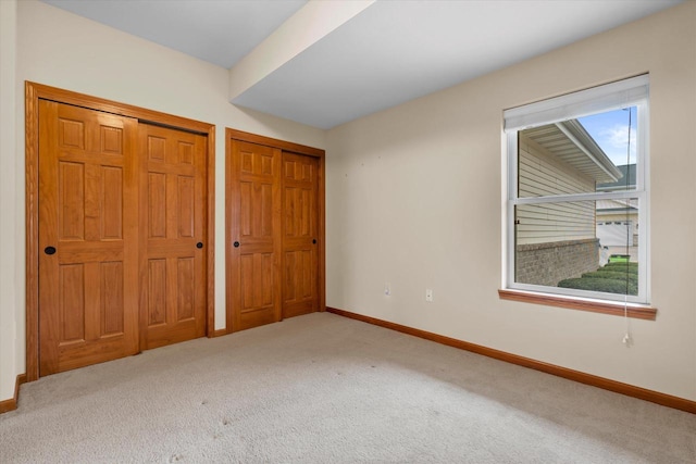 unfurnished bedroom with baseboards, carpet flooring, and multiple closets