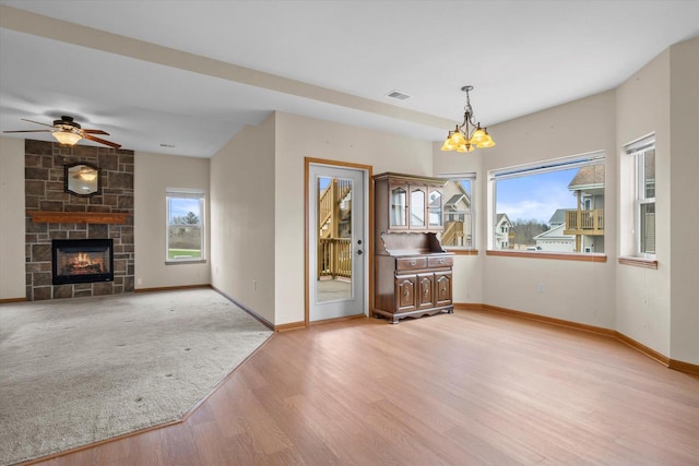 unfurnished dining area with light wood-style floors, ceiling fan with notable chandelier, a fireplace, baseboards, and visible vents