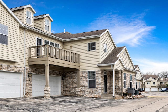 exterior space with central air condition unit, a garage, driveway, stone siding, and a balcony
