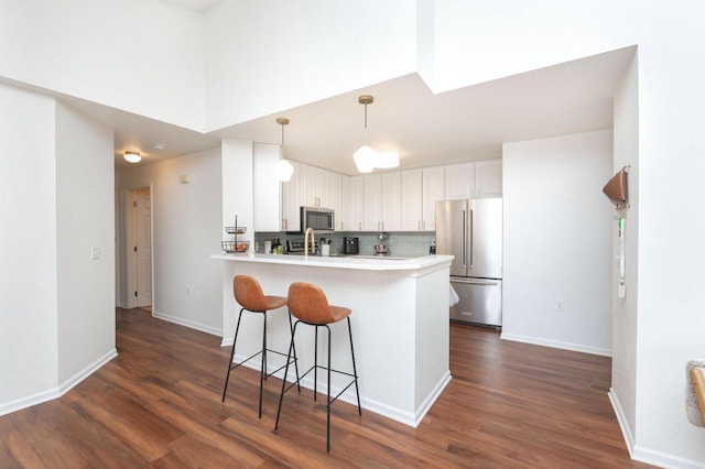 kitchen featuring dark wood-type flooring, a breakfast bar area, white cabinetry, a peninsula, and appliances with stainless steel finishes