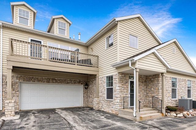 view of front of home featuring driveway, stone siding, central AC, a balcony, and an attached garage