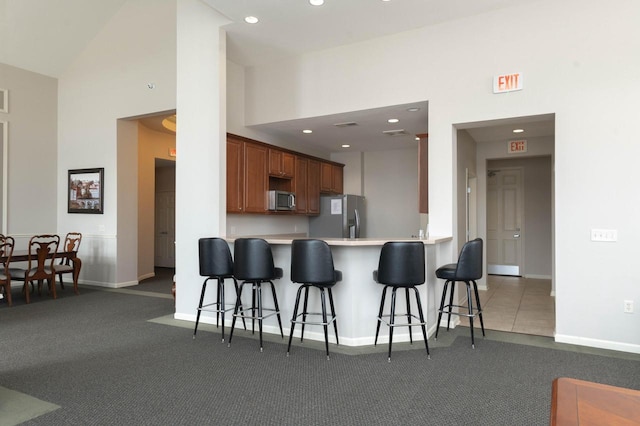 kitchen featuring stainless steel appliances, light countertops, a kitchen bar, baseboards, and a towering ceiling