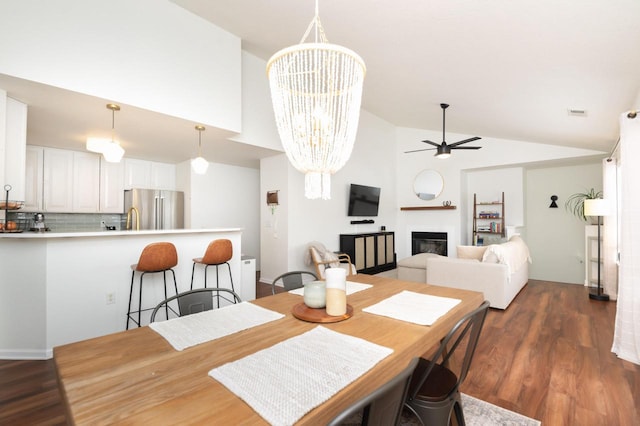 dining area featuring a glass covered fireplace, high vaulted ceiling, dark wood finished floors, and ceiling fan with notable chandelier