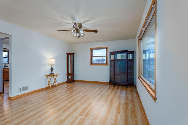 empty room with a sink, visible vents, baseboards, light wood-type flooring, and a ceiling fan
