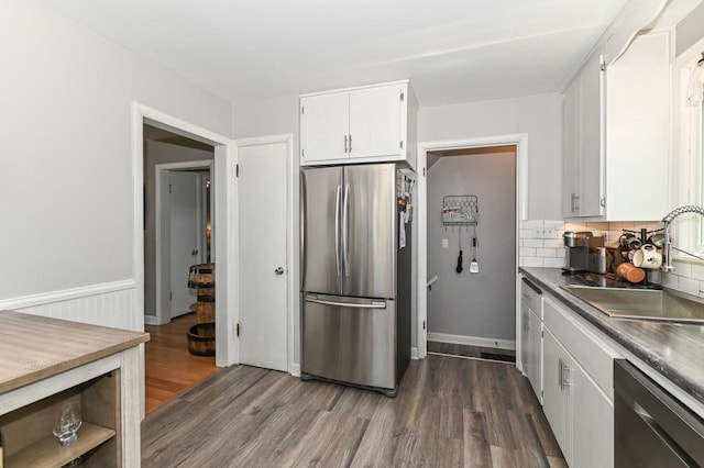 kitchen with decorative backsplash, stainless steel appliances, white cabinets, a sink, and dark wood-type flooring