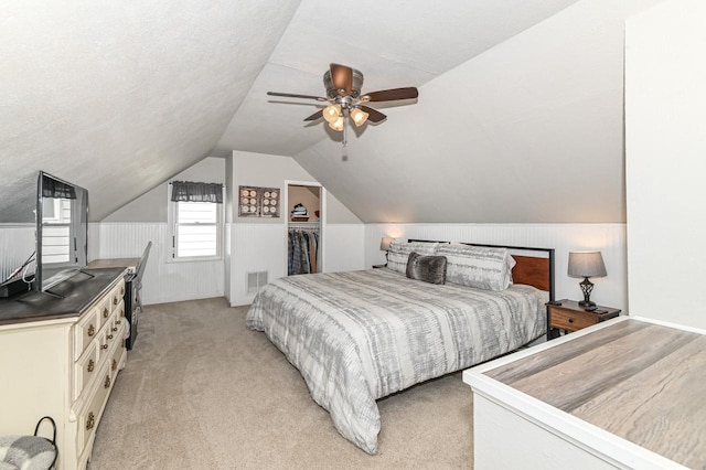 bedroom with ceiling fan, a wainscoted wall, visible vents, light carpet, and lofted ceiling