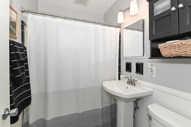 bathroom featuring toilet, a shower with curtain, visible vents, and wainscoting