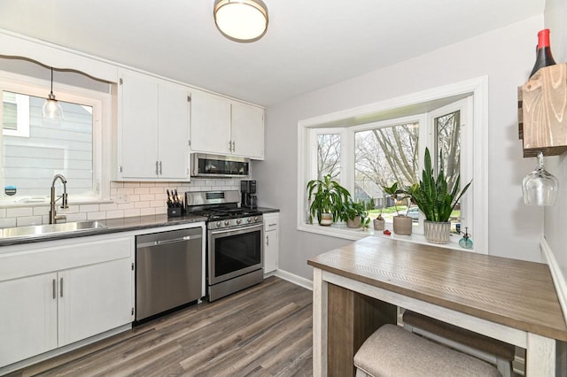 kitchen featuring dark wood-style floors, a sink, stainless steel appliances, backsplash, and white cabinetry