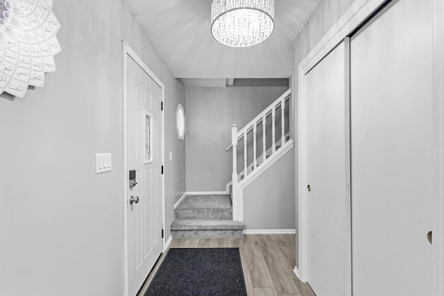 entrance foyer featuring an inviting chandelier, stairway, wood finished floors, and baseboards