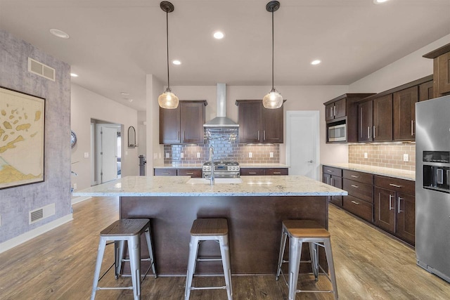402 Burnt Sienna Dr, Middleton, WI 53562 - kitchen with wall chimney range hood, appliances with stainless steel finishes, visible vents, dark brown cabinets, and wood finished floors