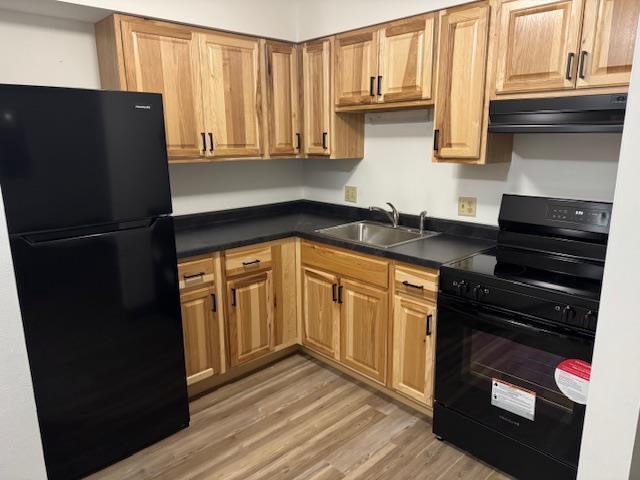 kitchen featuring a sink, light wood-style floors, dark countertops, black appliances, and range hood