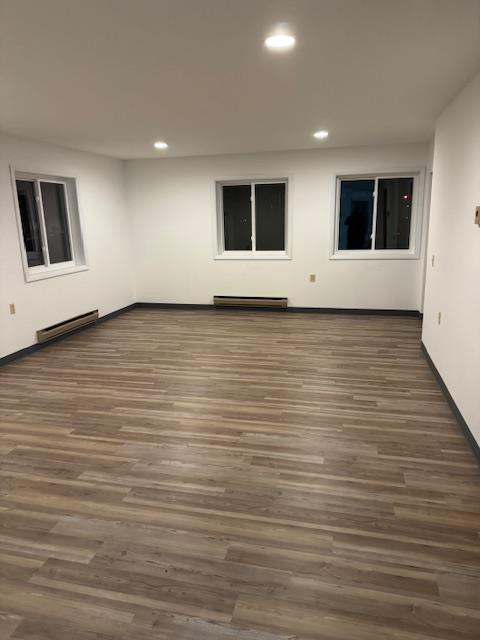 empty room with recessed lighting, wood finished floors, and a baseboard heating unit