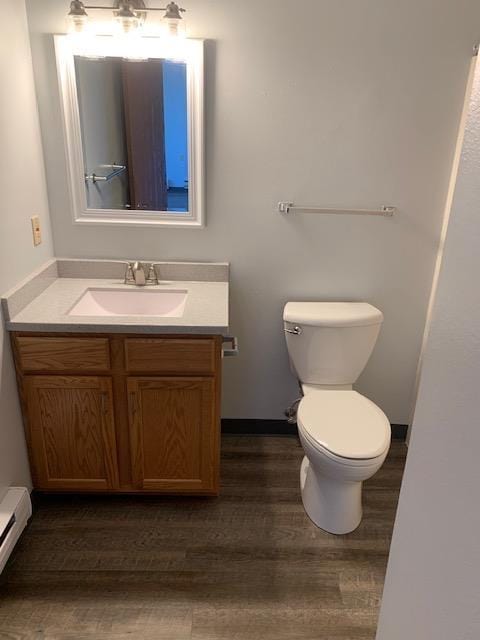 bathroom featuring wood finished floors, a baseboard radiator, toilet, vanity, and baseboards