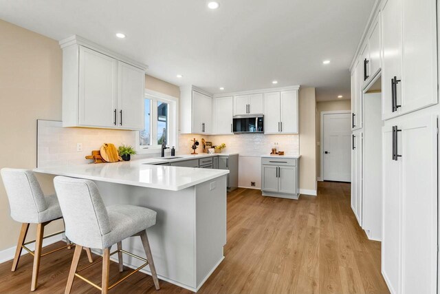 2352 Ryan Ave, Plymouth, WI 53073 - kitchen with a breakfast bar area, stainless steel microwave, decorative backsplash, light wood-type flooring, and a peninsula