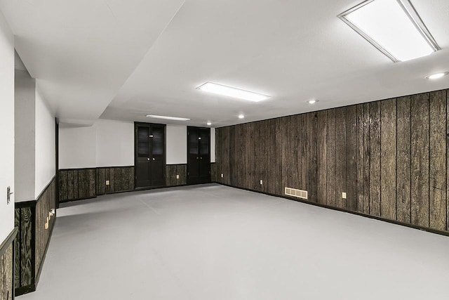 basement featuring recessed lighting, wood walls, visible vents, and a wainscoted wall
