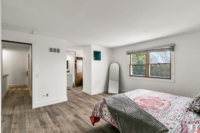 bedroom with baseboards, visible vents, wood finished floors, and attic access