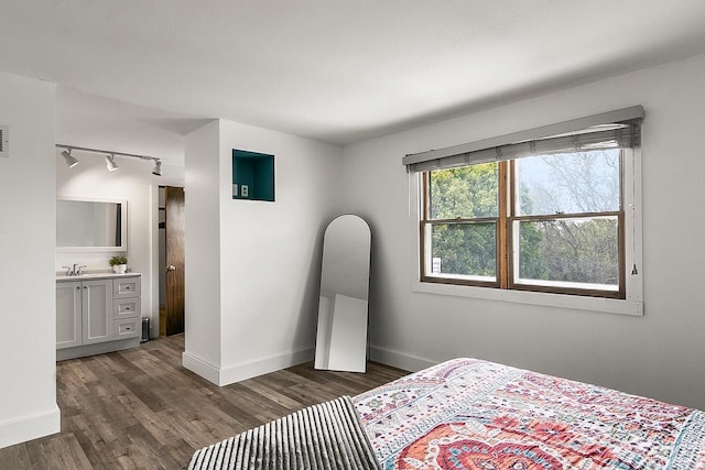 bedroom featuring baseboards, dark wood-style floors, track lighting, and a sink