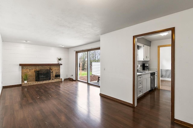 unfurnished living room featuring a sink, baseboards, a fireplace, and dark wood-type flooring