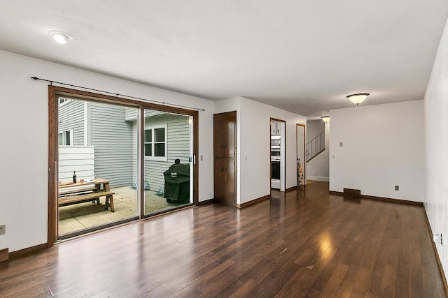 unfurnished living room with baseboards, stairway, and dark wood-type flooring