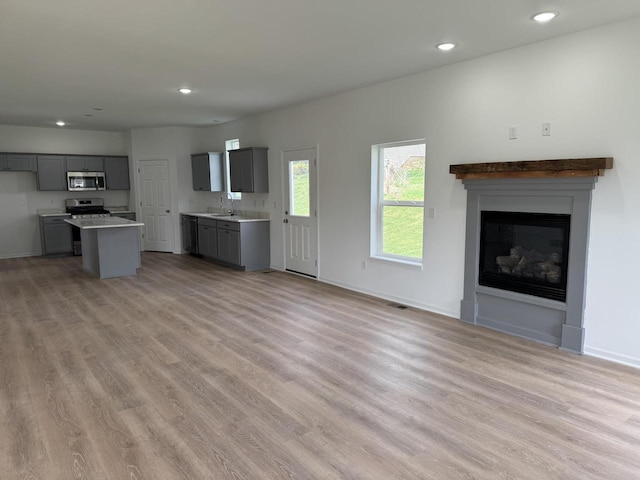 306 Filardo Ct, Mineral Point, WI 53565 - unfurnished living room with recessed lighting, a glass covered fireplace, baseboards, light wood-type flooring, and a sink