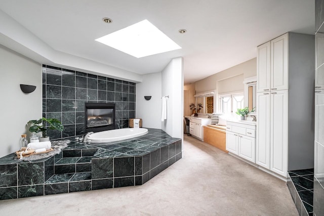 bathroom with a tiled fireplace, a skylight, a garden tub, and vanity