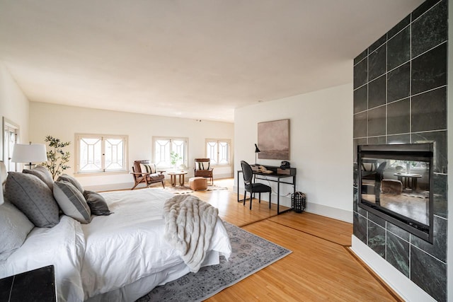 bedroom with a tile fireplace, light wood-style flooring, and baseboards