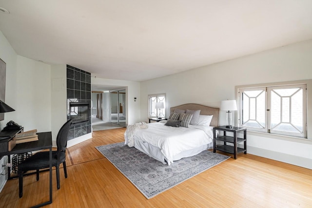 bedroom with a tile fireplace, light wood finished floors, and baseboards