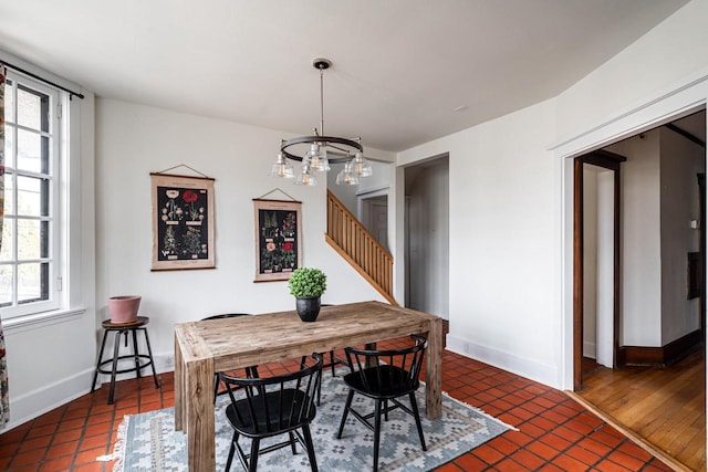 dining area featuring an inviting chandelier, baseboards, dark tile patterned floors, and stairs