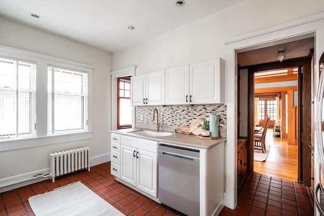 kitchen with stainless steel dishwasher, decorative backsplash, light countertops, radiator, and a sink
