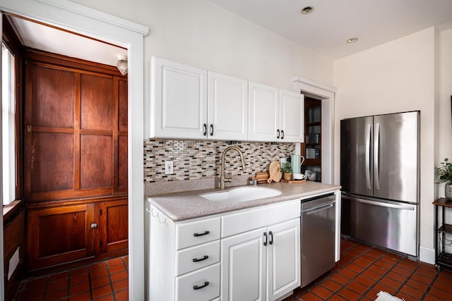 kitchen with tasteful backsplash, stainless steel appliances, light countertops, a sink, and white cabinetry