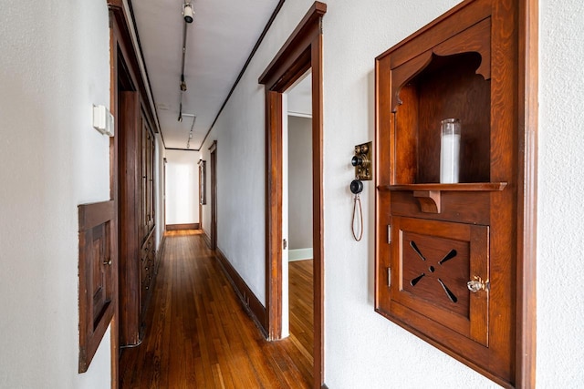 hallway featuring baseboards, rail lighting, and dark wood-type flooring