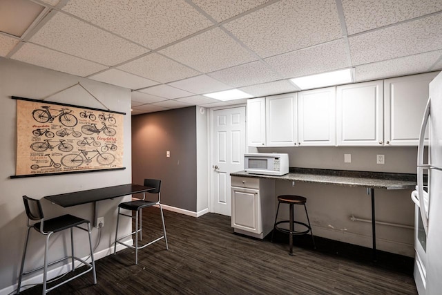 kitchen with a breakfast bar, white microwave, a drop ceiling, and dark countertops