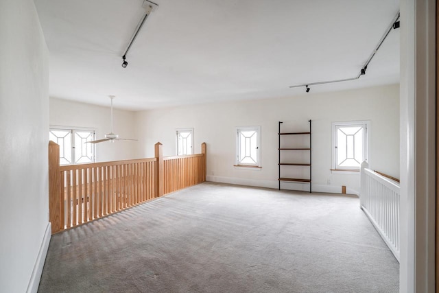 carpeted spare room with rail lighting, a ceiling fan, and baseboards