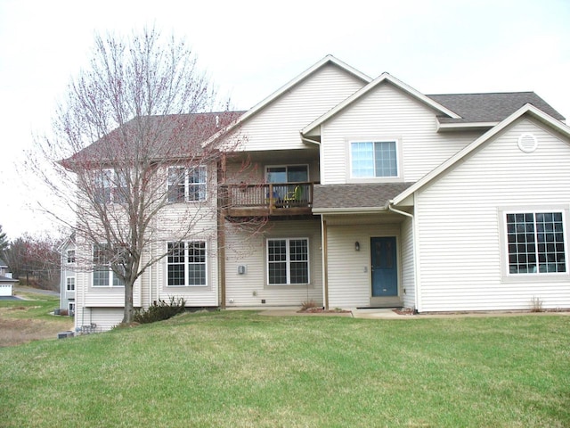 traditional-style home featuring a front lawn, a shingled roof, and a balcony