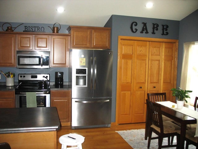 kitchen featuring light wood finished floors, brown cabinets, appliances with stainless steel finishes, and dark countertops