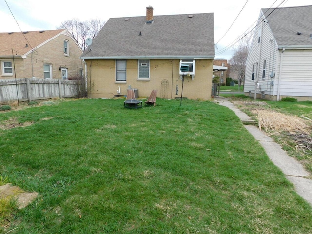 rear view of house with brick siding, a yard, a chimney, and fence