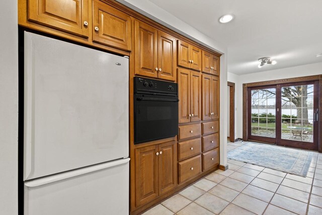 2108 Woodlawn Ln, Appleton, WI 54914 - kitchen featuring light tile patterned floors, white fridge, black oven, recessed lighting, and brown cabinetry