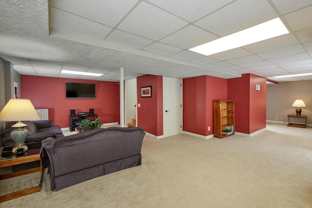 carpeted living area with a drop ceiling and baseboards