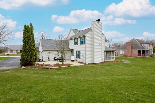 back of house featuring a chimney, a patio, a yard, and roof with shingles