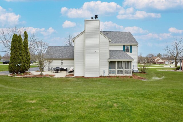 back of property with a chimney, a shingled roof, a sunroom, a patio area, and a lawn