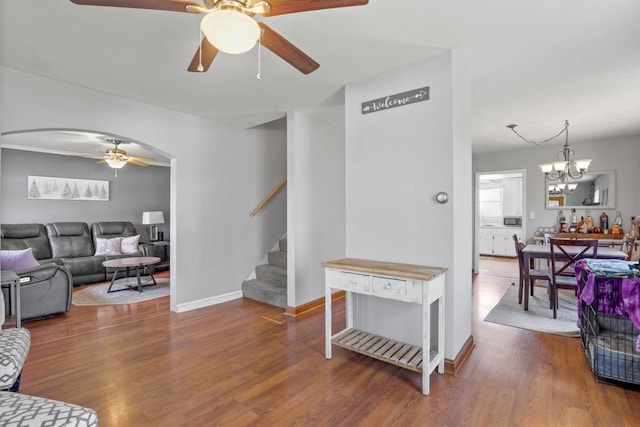 living area with stairs, baseboards, arched walkways, wood finished floors, and ceiling fan with notable chandelier
