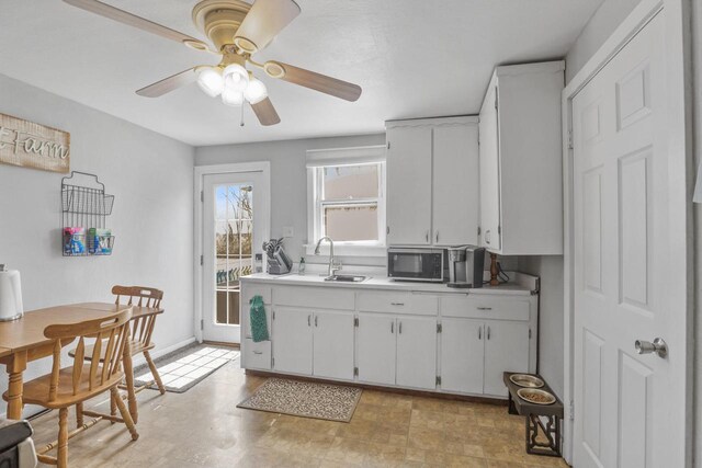 kitchen featuring stainless steel microwave, a sink, ceiling fan, light countertops, and white cabinets