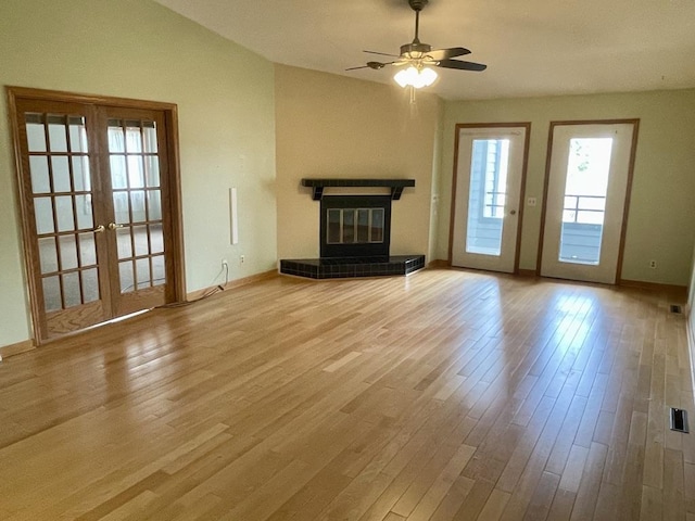 unfurnished living room featuring a tiled fireplace, a ceiling fan, baseboards, french doors, and wood finished floors