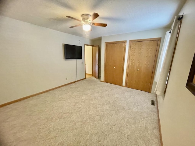 unfurnished bedroom featuring visible vents, baseboards, carpet floors, two closets, and a ceiling fan