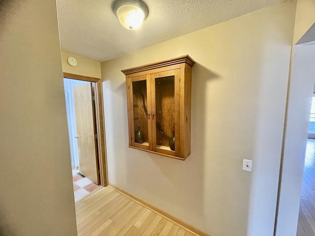 hall with a textured ceiling, light wood-style floors, and baseboards