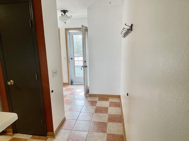 hall with light tile patterned floors, a textured wall, and baseboards