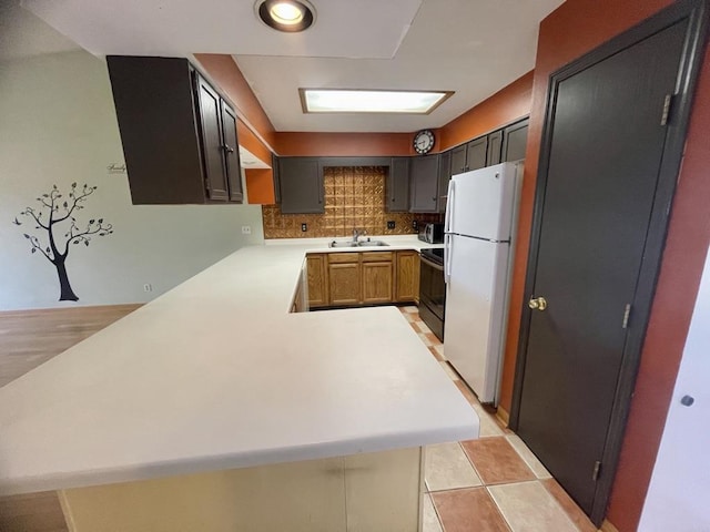 kitchen featuring tasteful backsplash, light countertops, freestanding refrigerator, a peninsula, and black / electric stove