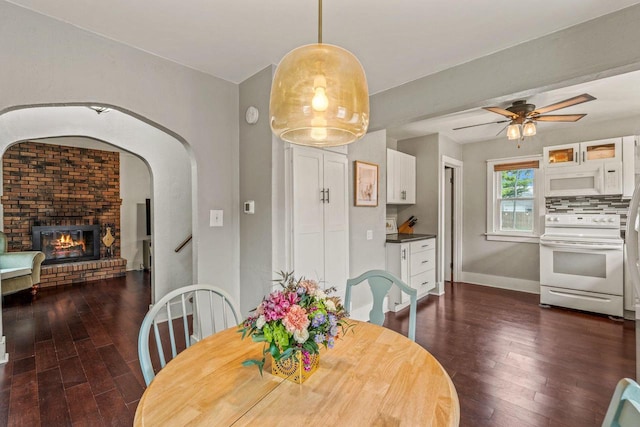 dining area with a fireplace, dark wood-style flooring, ceiling fan, and baseboards
