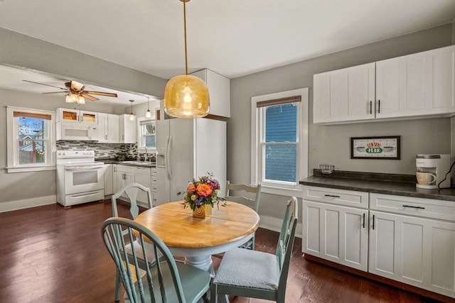 dining room with a wealth of natural light, a ceiling fan, dark wood-type flooring, and baseboards