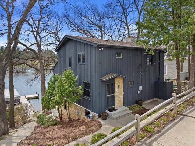 modern farmhouse style home featuring board and batten siding, a chimney, a water view, a shingled roof, and fence